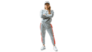 Sassy sportswear woman in gray athletic tracksuit and white sneakers, standing with arms crossed, black background, modern casual activewear, confident sporty fashion, Tuki version 03, lifestyle, fitness attire, casual athletic clothing, dynamic pose.
